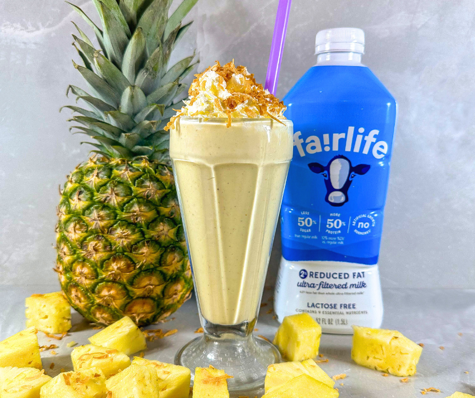A tall glass filled with caramelized pineapple smoothie and topped with whipped cream and toasted coconut