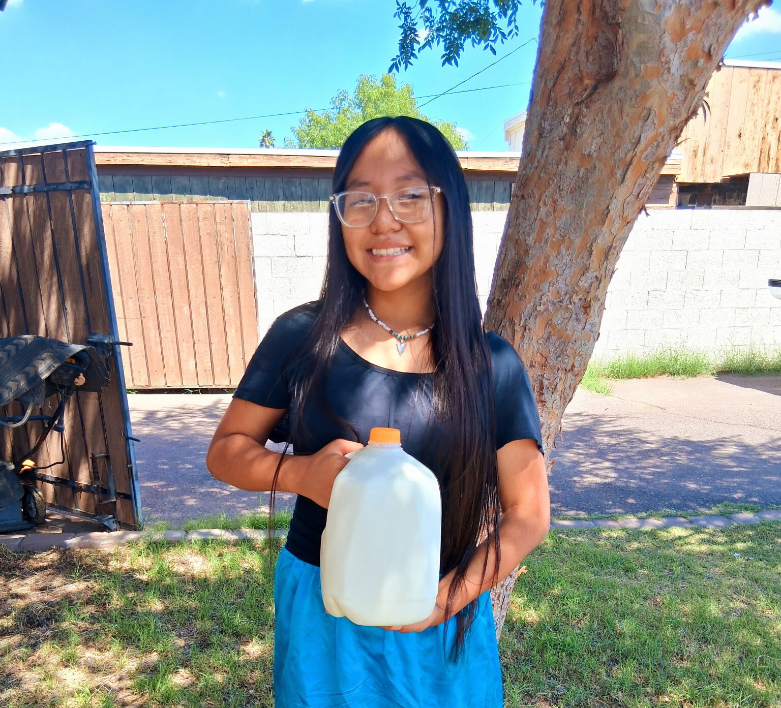 Photo of Native American girl standing outside holding a gallon of milk.